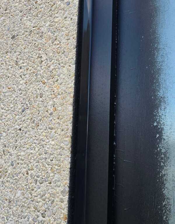 Close-up of freshly injected black commercial caulking compound inside a cleaned window joint channel on an aggregate stucco wall in Burlington.