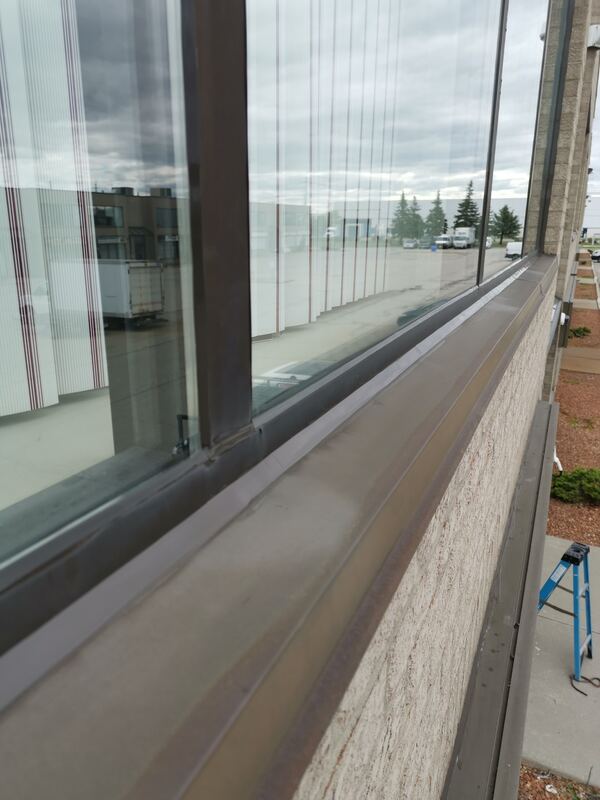 Close-up of a flawlessly finished, straight commercial sealant bead on a bronze window frame sill in Burlington.