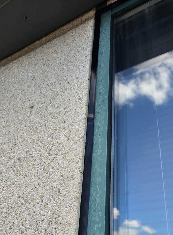 Close-up of a flawlessly finished, paintable commercial sealant bead around a window frame on an aggregate stucco wall by Proper Caulking in Burlington.