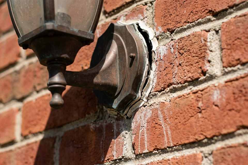 Failed exterior light fixture caulking at outdoor sconce base plate on Oakville brick home showing open perimeter gap and moisture staining.