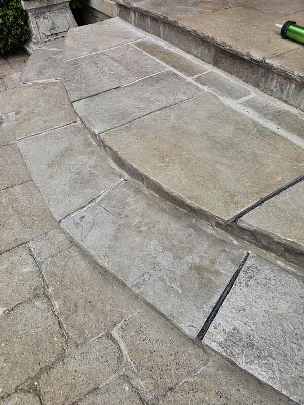 Angle view of stone flagstone porch steps showing clean joint gaps on the left and black closed-cell foam backer rods packed into the deep channels on the right.