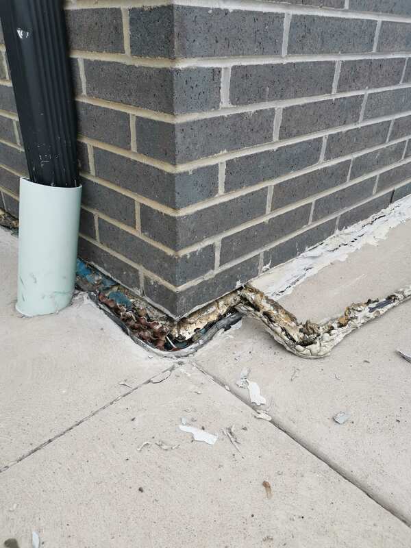 Close-up of rotted foam backing material and old decayed sealant being scraped out of a concrete to brick foundation joint cavity.