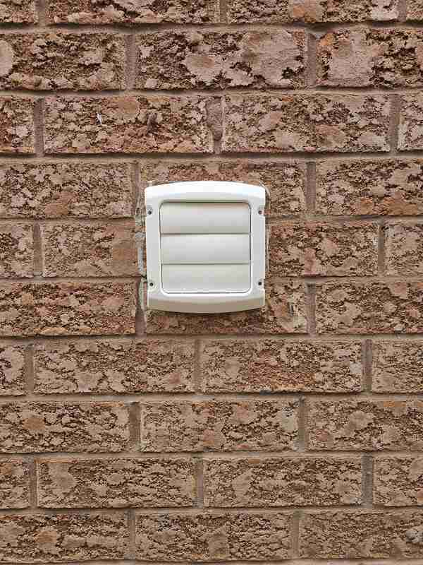 Close-up view of a brand-new white plastic louvered dryer vent hood mounted flush against a red brick exterior wall facade.