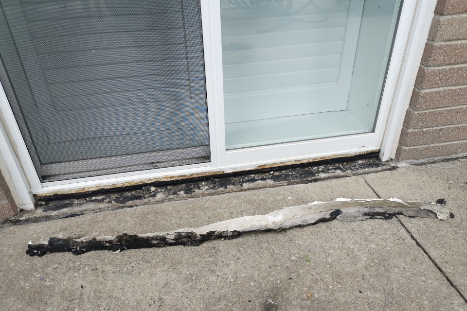 Old brittle caulking peeled away from a residential door frame during repair by Proper Caulking in Burlington.