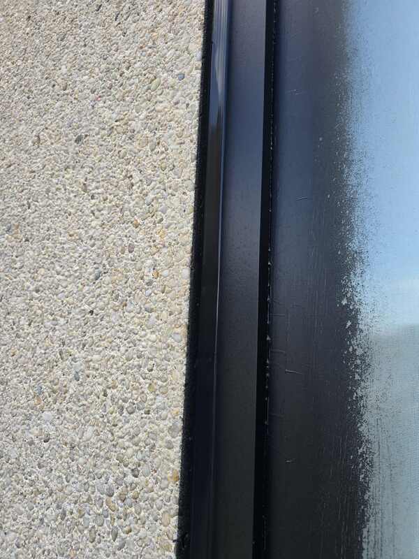 Close-up of a dark foam backer rod packed into a window joint channel next to newly applied commercial caulking on an aggregate wall.