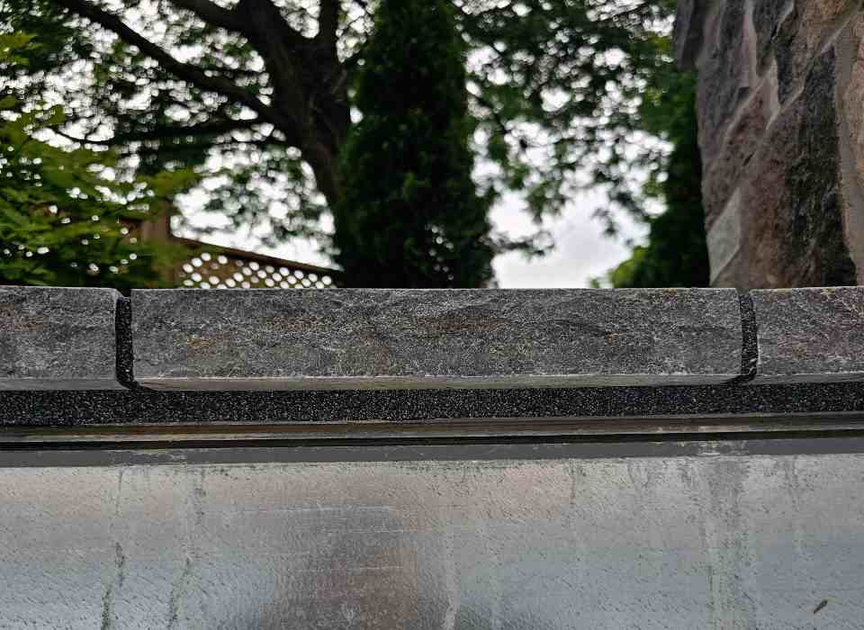 Straight-on view of a natural stone pool coping ledge showing black foam backer rods packed tightly into both the horizontal and vertical masonry joint gaps.