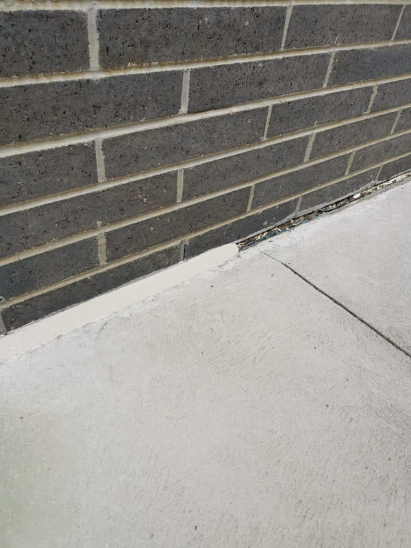 Close-up of a gray foam backer rod inserted into a foundation expansion joint next to a newly applied line of tan silicone sealant.