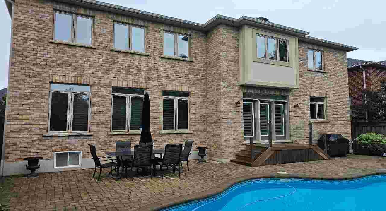 Rear exterior view of a two-story brick home in Burlington featuring a swimming pool, patio, and newly caulked tan windows by Proper Caulking.