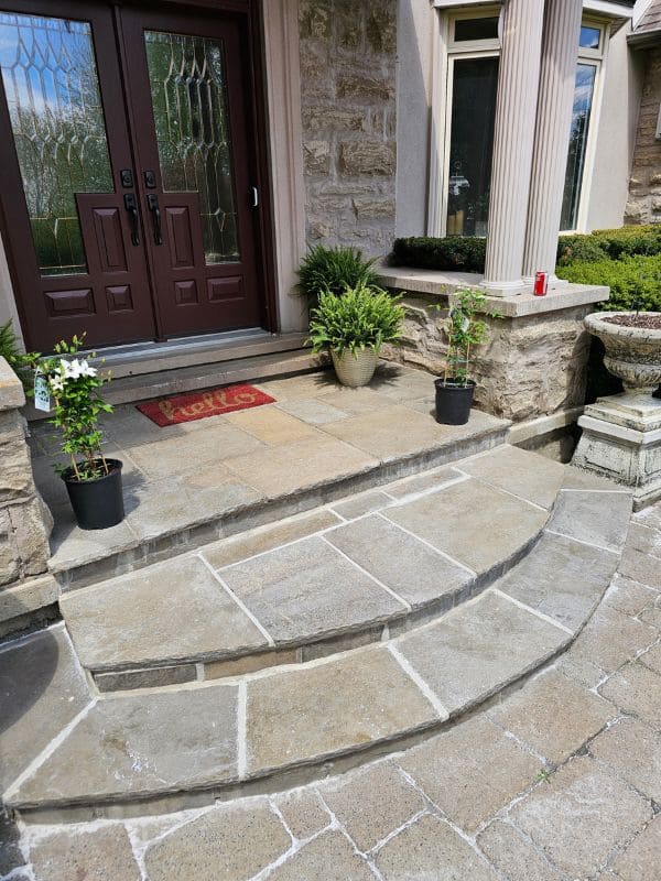Wide angle view of completed, flawlessly sealed natural flagstone entry steps and front porch landing of a luxury brick and stone house.