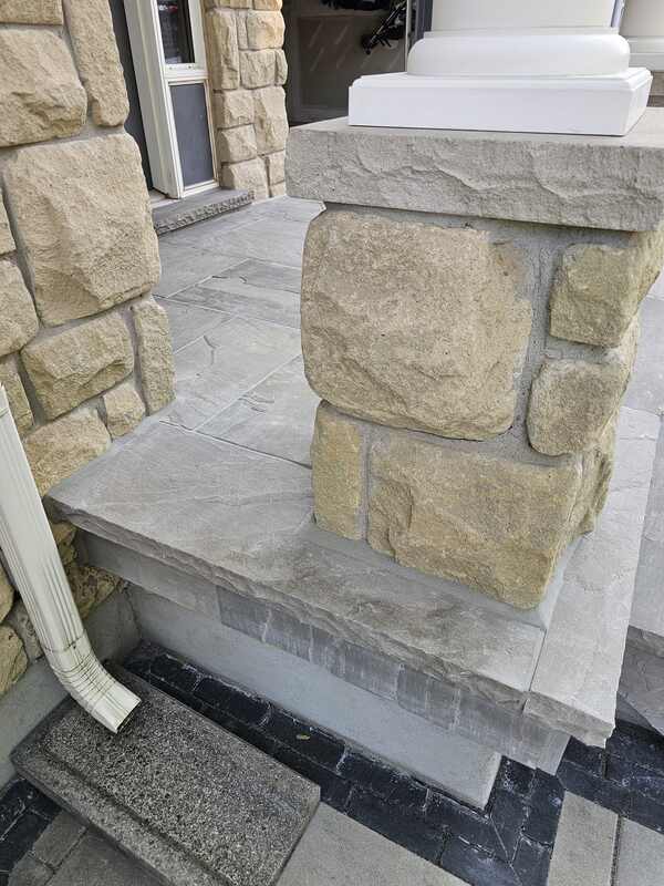 Side angle view of a completed, flawlessly sealed natural flagstone porch entryway and stone columns with texturized matte grey sealant joints.