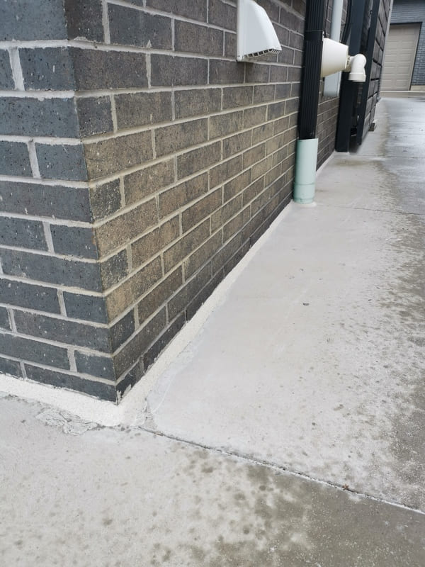 Close-up of a perfectly tooled, uniform tan silicone sealant bead completely protecting a grade-level concrete foundation expansion joint.