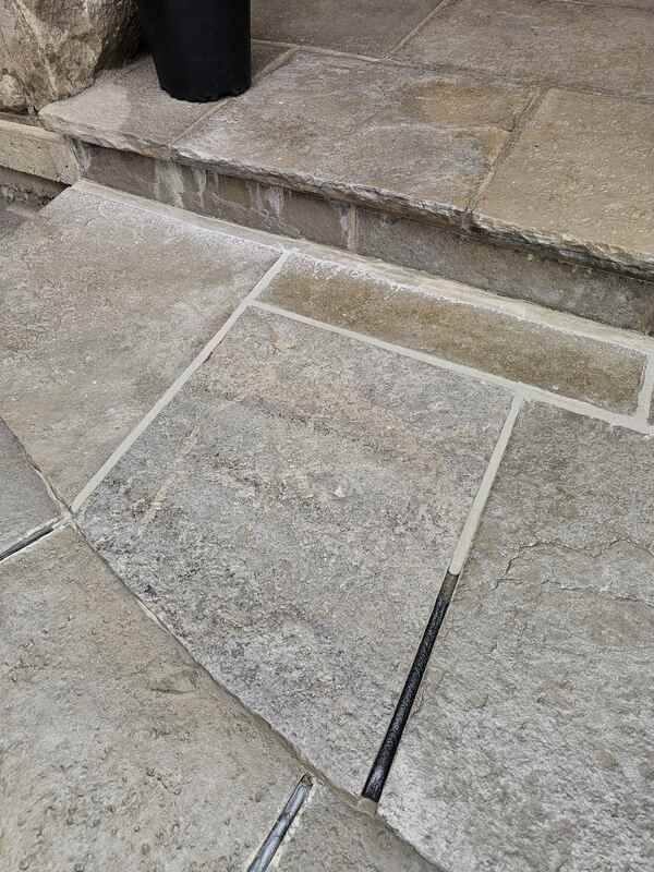 Close-up of natural stone flagstone porch steps showing a black backer rod deep in a joint next to completed, perfectly tooled grey silicone sealant seams.