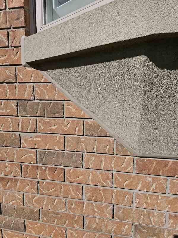 Close-up of a flawlessly tooled tan silicone expansion joint sealing the angled transition line between a sand-textured stucco architectural projection and a red brick home wall.