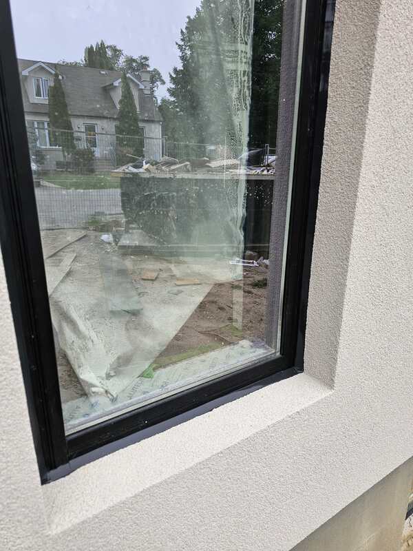 Close-up of a perfectly tooled and smooth black silicone sealant bead sealing the perimeter interface between a black vinyl window frame and a light grey stucco wall.