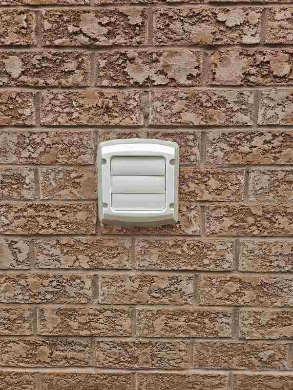 Macro close-up view of a brand-new white dryer vent exhaust hood flawlessly sealed against a red brick wall with a tooled grey silicone bead.