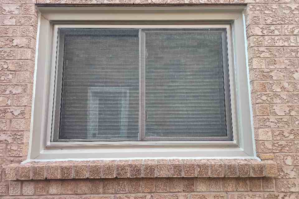 Close-up of a newly applied and perfectly smoothed tan silicone sealant bead sealing the perimeter of a vinyl window frame against a brick home exterior wall.