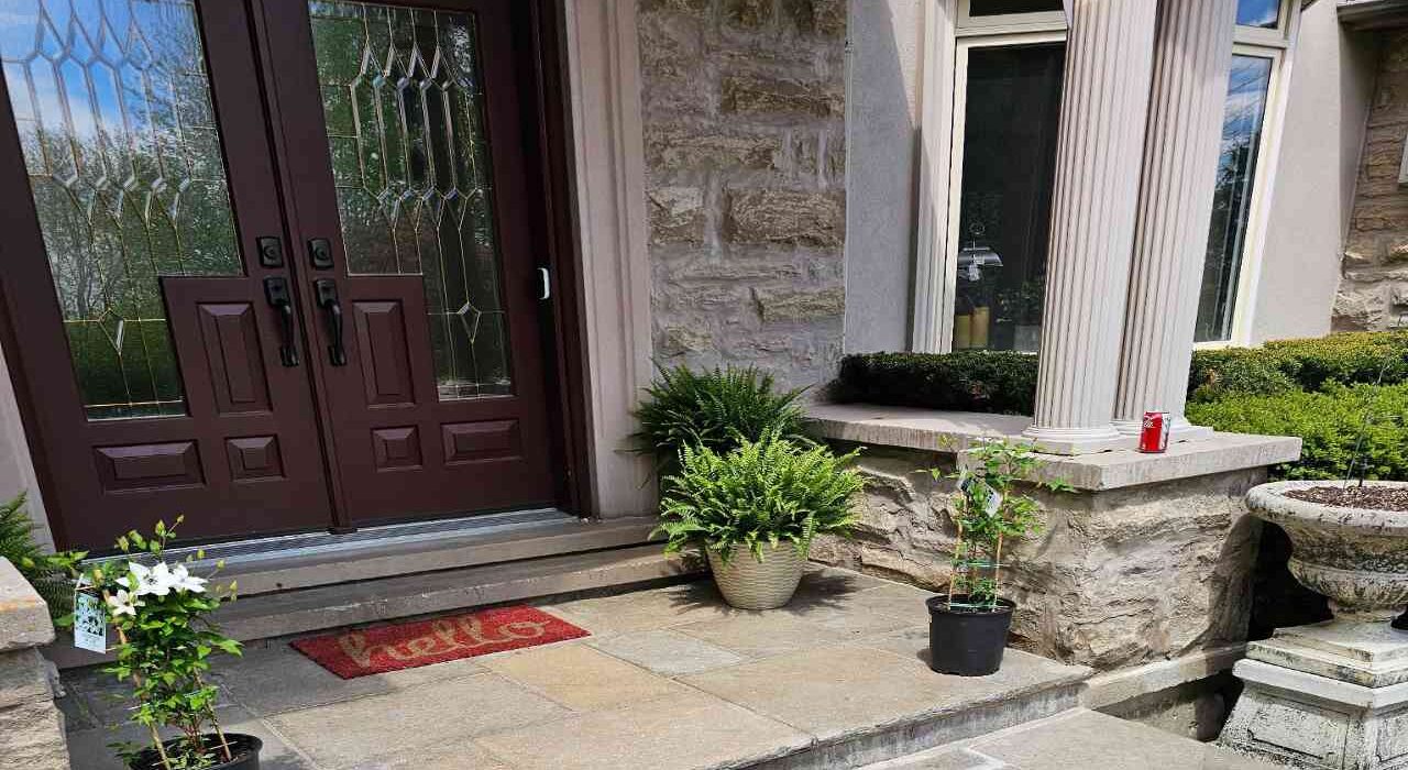 Front entry porch of a luxury house featuring a dark wood double door, natural stone masonry walls, flagstone landing slabs, and large structural columns.