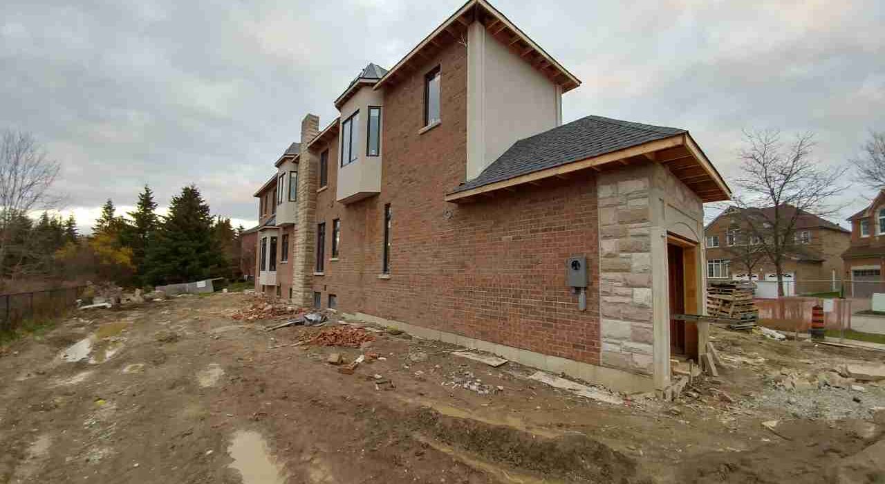 Exterior side view of a large custom brick and stone home under construction featuring newly installed and sealed window frames.