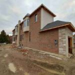 Exterior side view of a large custom brick and stone home under construction featuring newly installed and sealed window frames.