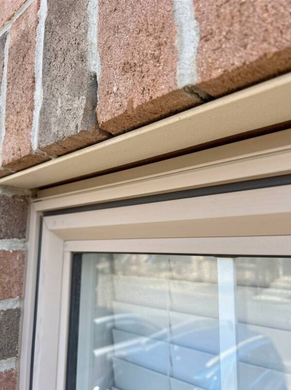 Close-up of a flawlessly applied and smoothed tan silicone sealant bead protecting the joint below a brick window lintel.