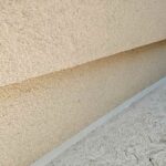 Long angled view of a flawlessly tooled tan silicone expansion joint seal along a modern residential stucco foundation wall and textured concrete walkway.