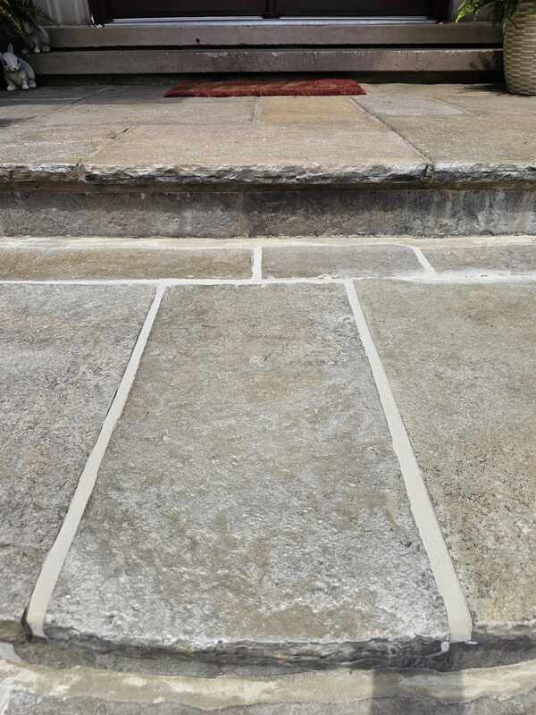 Straight-on close view of natural flagstone steps with newly applied, smooth tan architectural caulking seams running between the stone blocks.