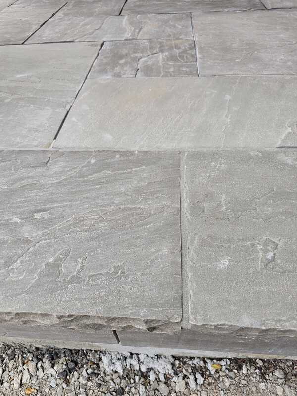 Close-up view of premium grey flagstone steps showing completely raw, empty, and open horizontal joint channels before sealant application.