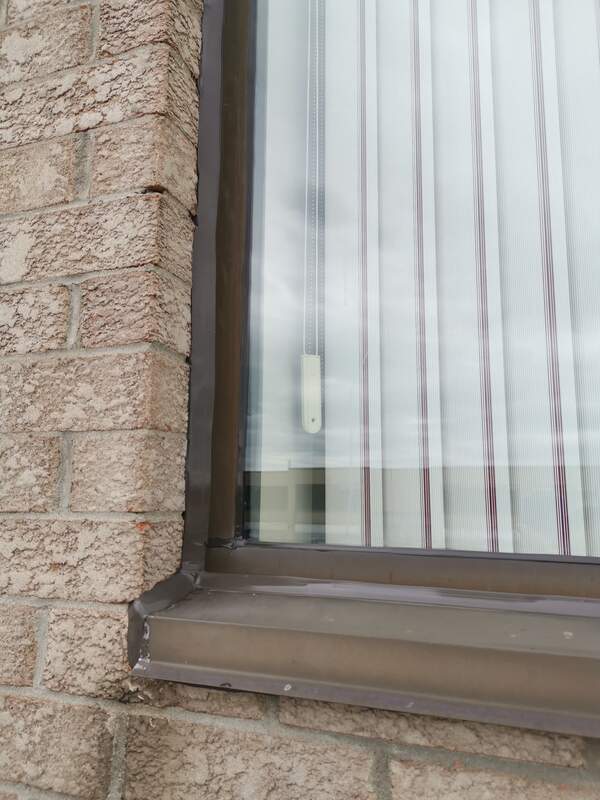 Close-up of a completed, flawlessly smooth commercial-grade sealant bead on a bronze window frame and brick wall in Burlington.