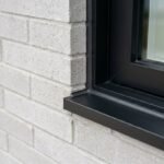 A crisp, professionally dry-tooled dark charcoal sealant joint applied smoothly between light grey brick masonry and a matte black aluminum window frame casing on a modern residential home.
