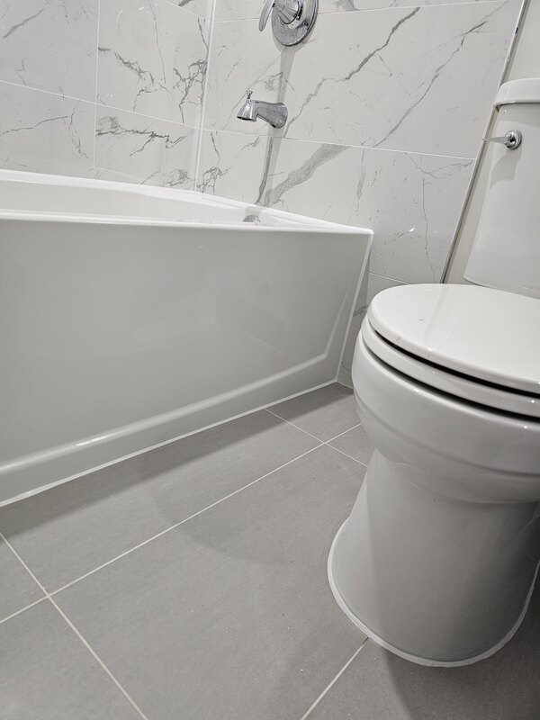 A view of a completed bathroom caulking job showing a flawless white silicone bead along the bathtub base, tile floor, and toilet perimeter.