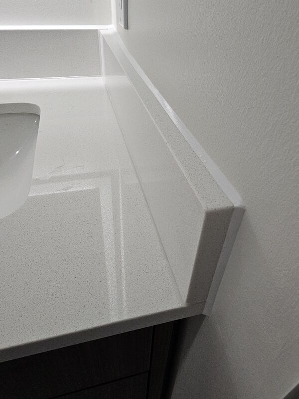A close-up side angle of a bathroom vanity showing a flawless white silicone caulking bead sealing a stone side-splash to a painted wall.