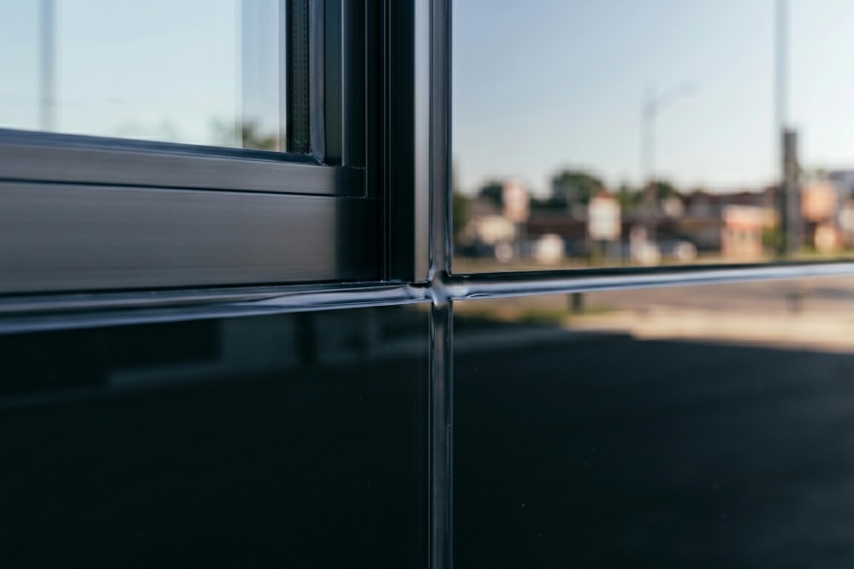 An immaculate, continuous cross-junction of tooled black silicone sealant on an anodized aluminum frame and commercial glass facade panel.
