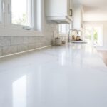 A wide close-up landscape view of a completed kitchen backsplash sealing job showing a flawless white silicone bead along a quartz countertop joint.