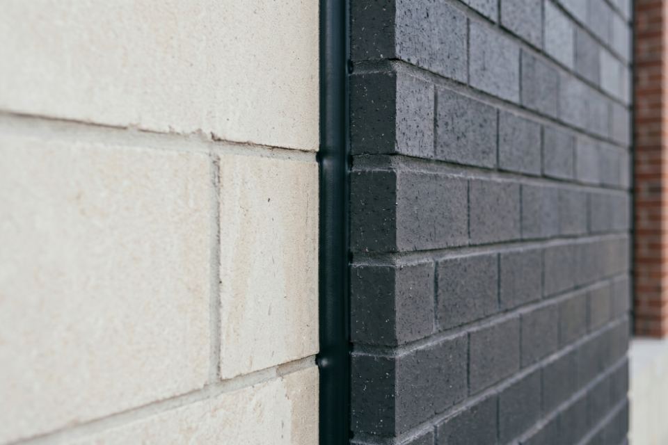An immaculate, neatly tooled concave bead of black polyurethane sealant sealing a vertical expansion joint between precast stone and charcoal brick masonry.