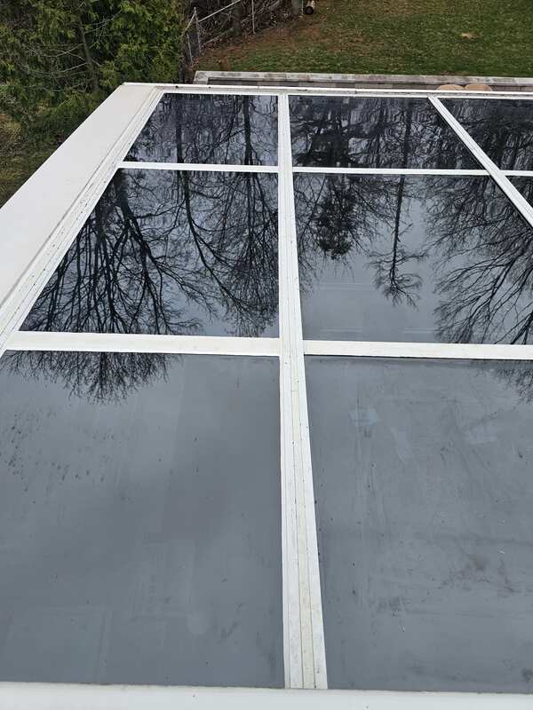 Completed glass roof caulking showing a clean white commercial sealant bead bonding an insulated glass pane to a sloped white aluminum frame sash.
