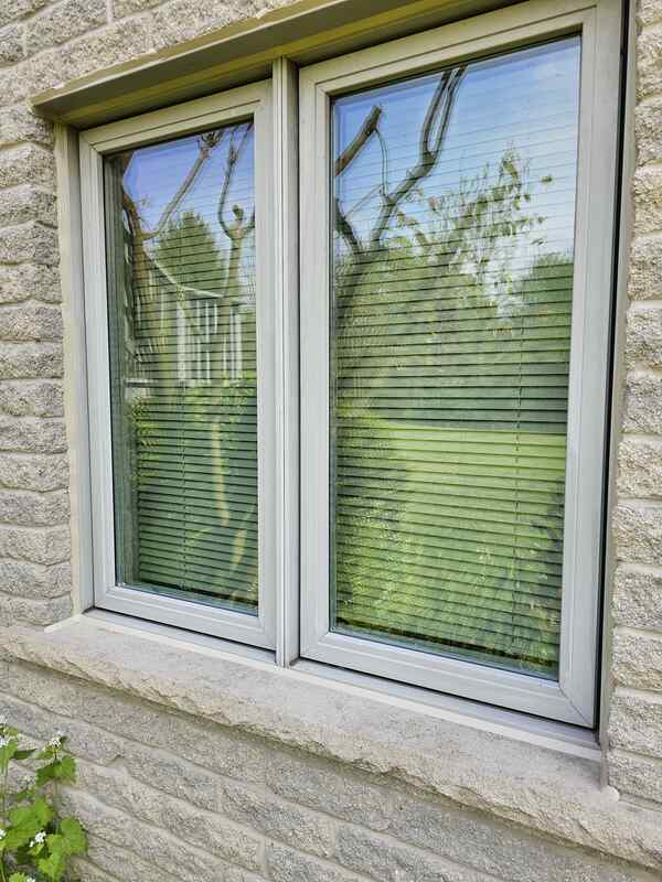 A close-up view of an exterior split-faced masonry wall showing a completed window flashing caulking job on a metal drip cap above a vinyl frame.
