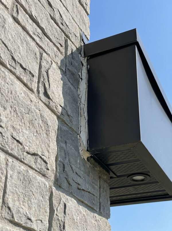 Failed exterior soffit caulking showing cracked, thin retail sealant pulling away from a residential split-face stone wall facade.