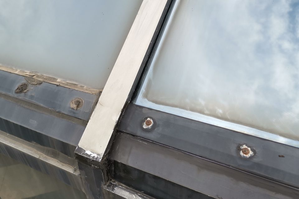 Close-up view of a failed exterior skylight perimeter sealant line showing cracked, lumpy caulking and rusted frame screws on a residential roof.