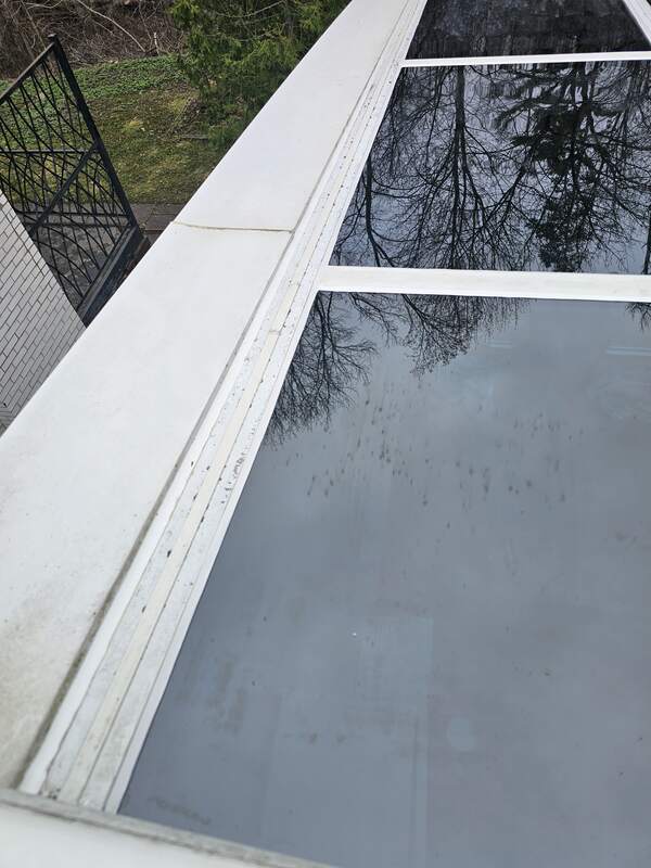 Failed glass-to-frame caulking showing a dirty, cracked, and dried-out white sealant line on a sloped glass skylight panel.