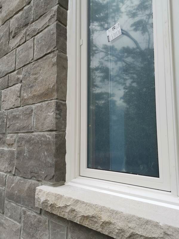Completed window caulking showing a crisp white commercial sealant bead bonding a vinyl window frame to a rough grey stone masonry wall.