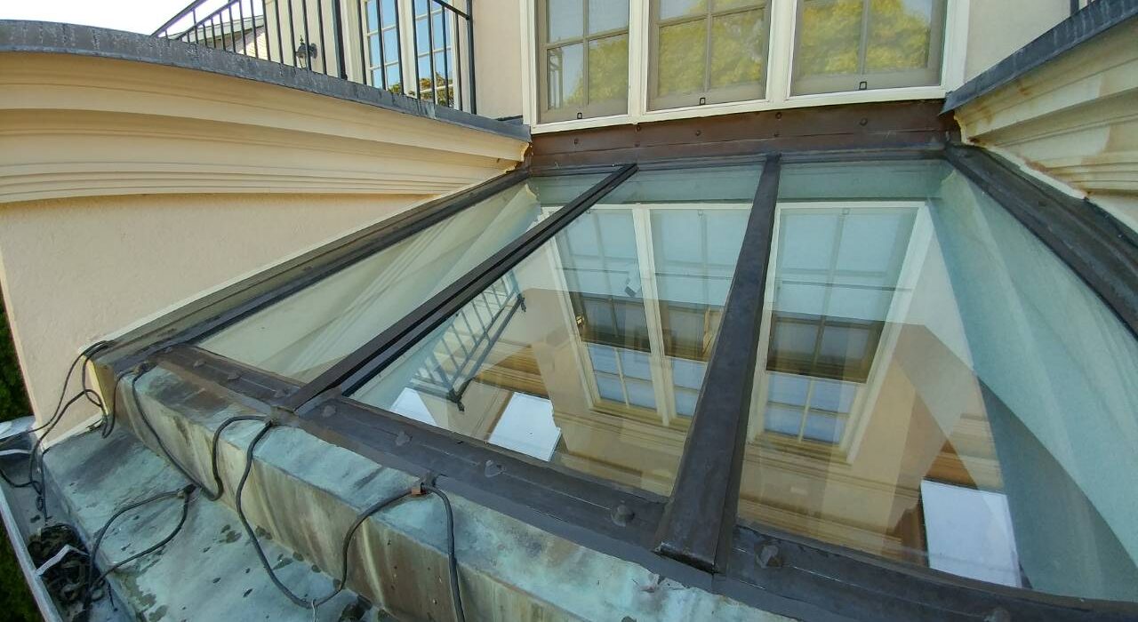 Angle view of a premium multi-panel exterior skylight glass roof assembly with bronze framing and copper flashing details on a luxury home facade.