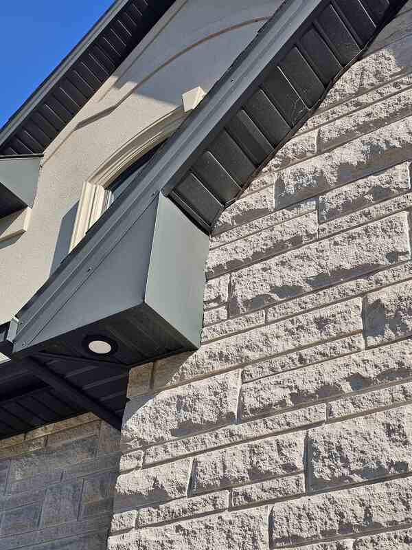 Looking up at a premium black aluminum eave soffit panel intersection flawlessly caulked against a luxury stone and stucco residential home facade.