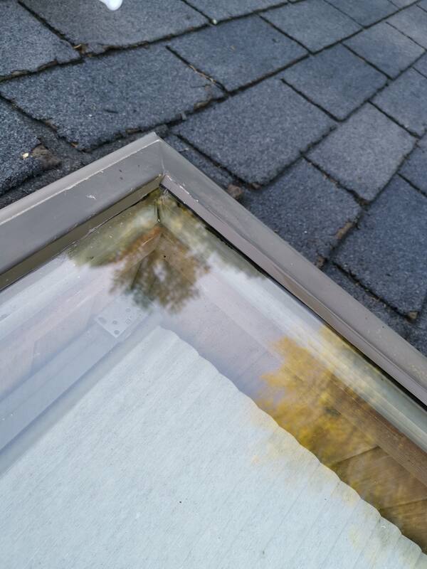 Close-up view of a residential skylight glass corner on an asphalt shingle roof with all old sealant mechanically extracted down to a clean channel.