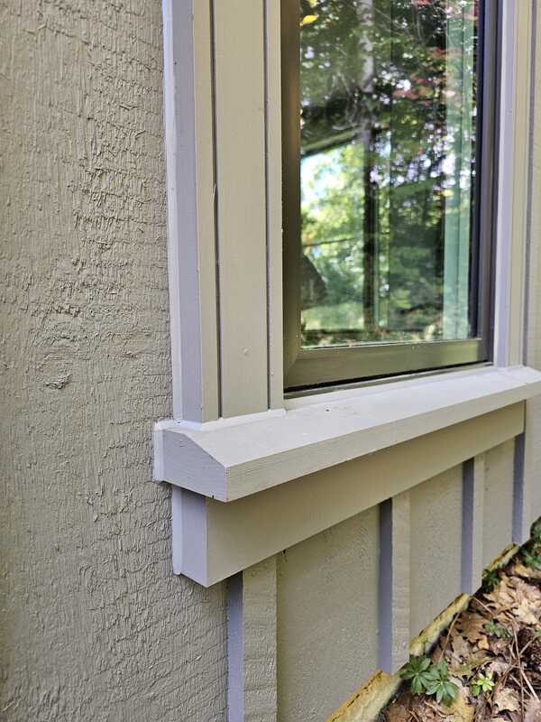 A close-up view of a completed exterior caulking job showing a clean grey polymer bead sealing a window casing trim frame to textured composite vertical siding.