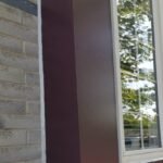 A crisp vertical white elastomeric sealant joint applied flawlessly into the mortar gaps of a grey brick wall and a smooth brown wood window trim casing.