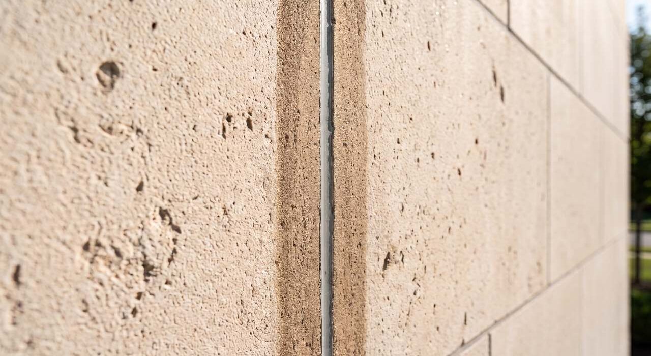 A side-angle view of an exterior limestone facade showing a uniform, 2-inch parallel band of dark oil staining caused by caulk bleeding on light stone.