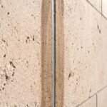 A side-angle view of an exterior limestone facade showing a uniform, 2-inch parallel band of dark oil staining caused by caulk bleeding on light stone.