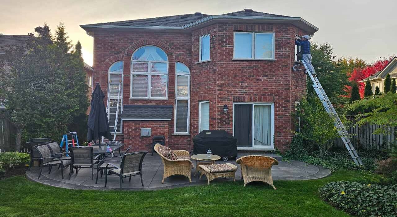 Exterior caulking Burlington home project showcasing professional window frame perimeter sealing from an extension ladder.