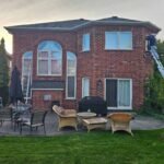 Exterior caulking Burlington home project showcasing professional window frame perimeter sealing from an extension ladder.
