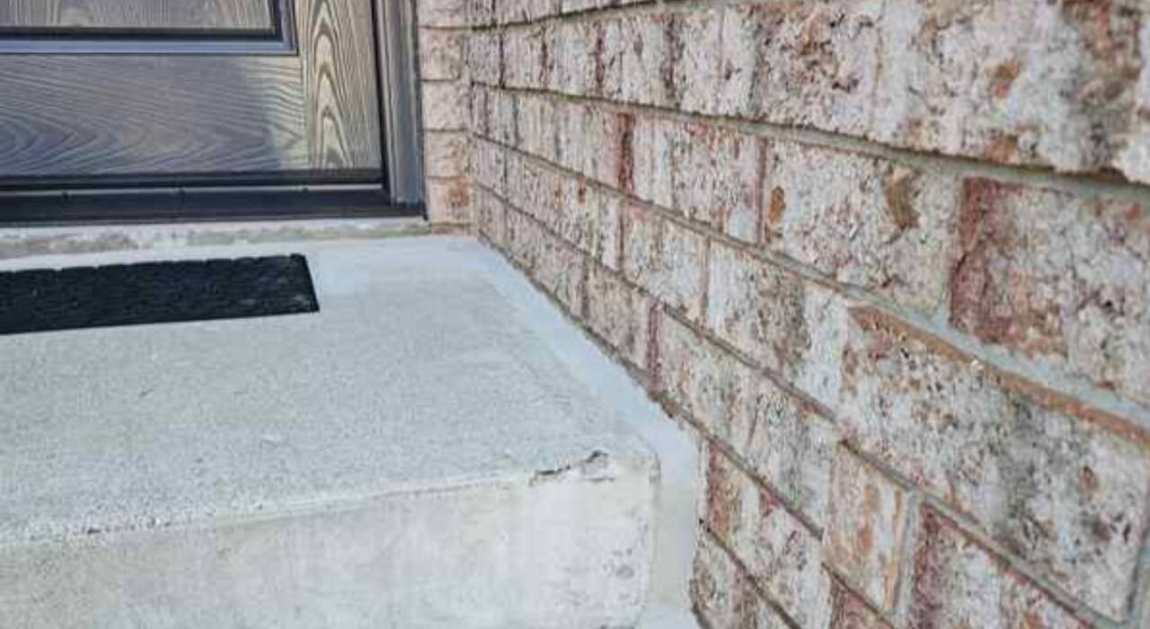 A pristine, freshly tooled exterior caulking joint sealing a concrete porch landing pad against a red clay brick masonry wall.